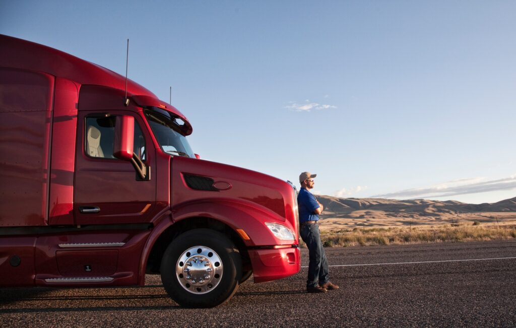 Truck driver leaning on the grill of his commercial truck.